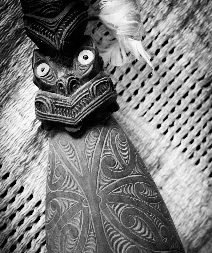 Carved wooden taiaha with pāua eyes on a woven whāriki